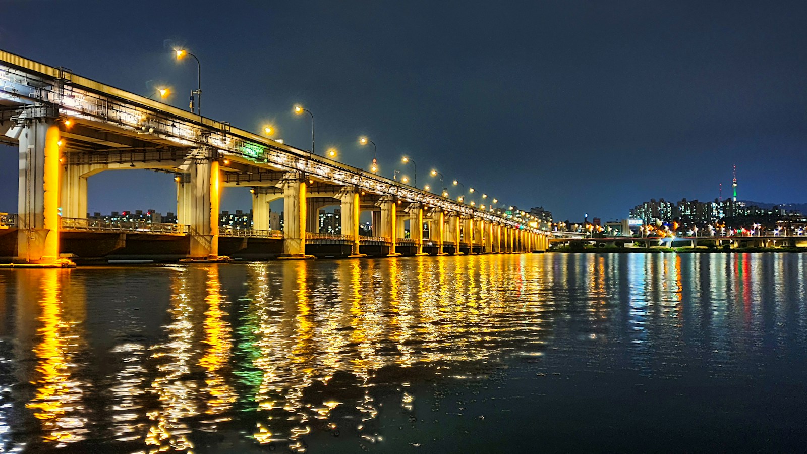 Banpo Bridge lit up over the Han River at night, with N Seoul Tower in the distance