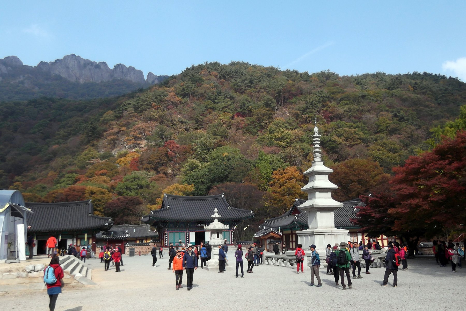 Visitors in the courtyard of Naejangsa temple with autumn colours on the hills behind