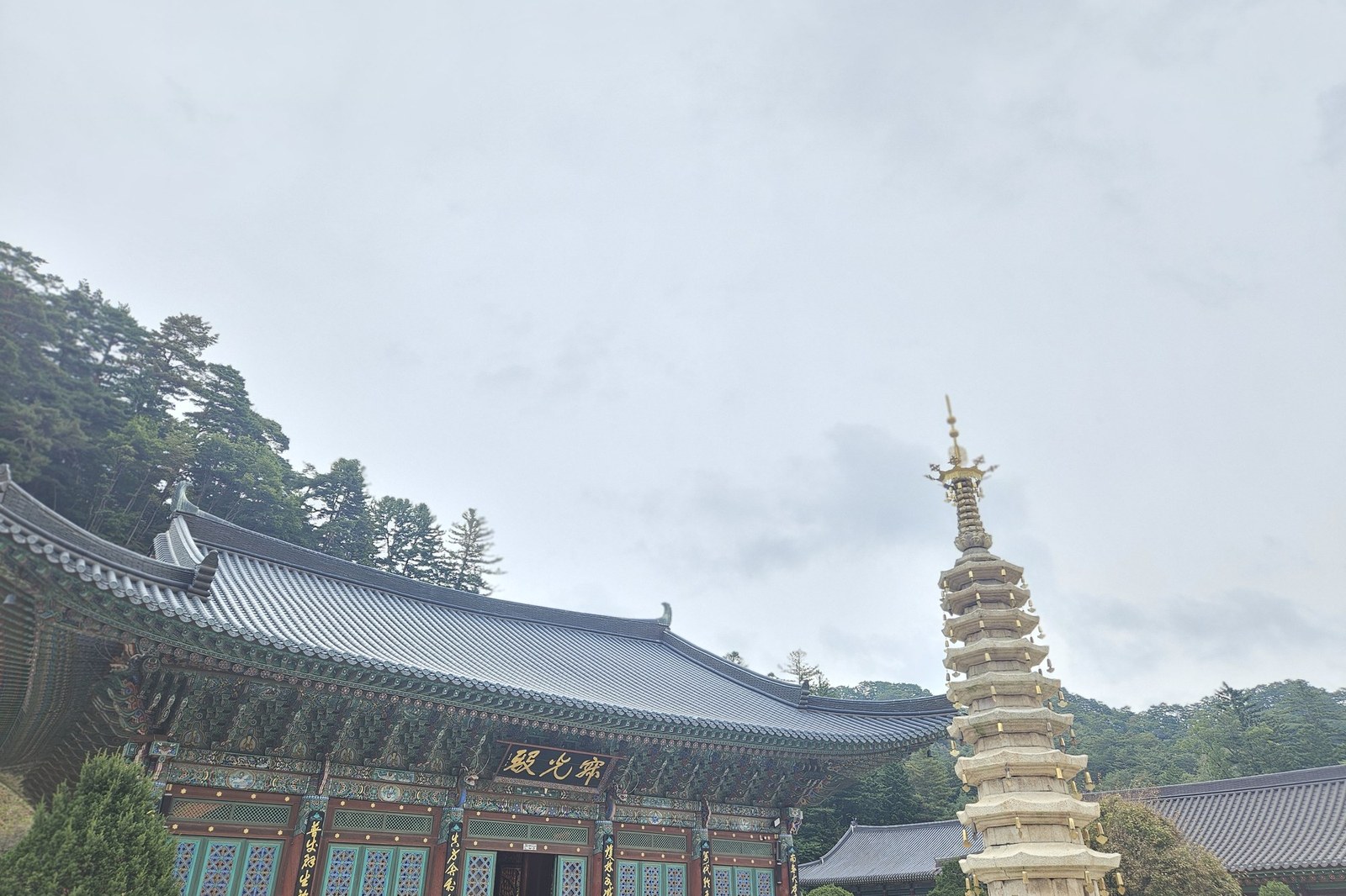 The main hall of Woljeongsa Temple with a painted wooden roof and the tall octagonal nine-story stone pagoda in front, under an overcast sky