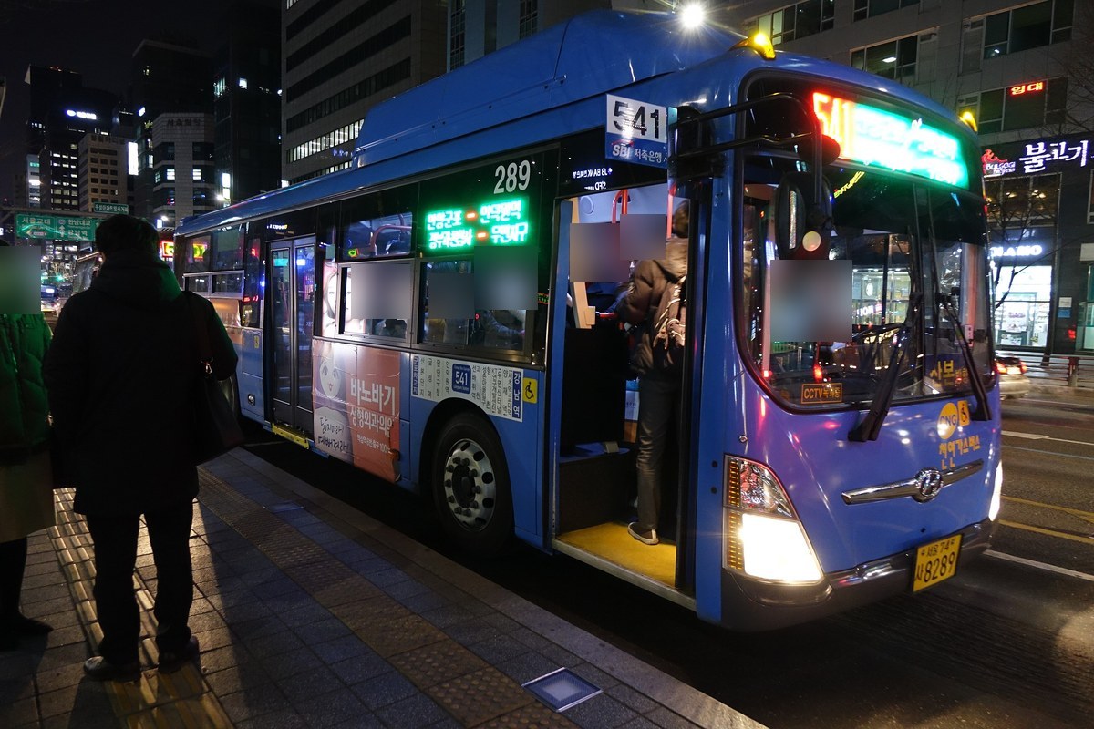 Passengers boarding a blue Seoul city bus at a roadside stop at night