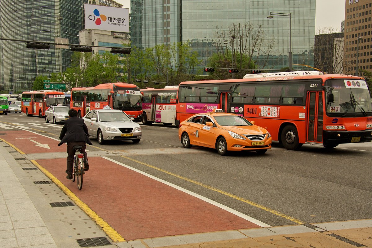 An orange Seoul taxi driving past red buses on Sejong-daero in central Seoul