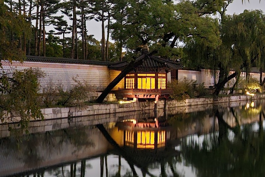Hahyangjeong, a small wooden pavilion at the edge of the Gyeonghoeru pond, glowing yellow through its paper doors at night