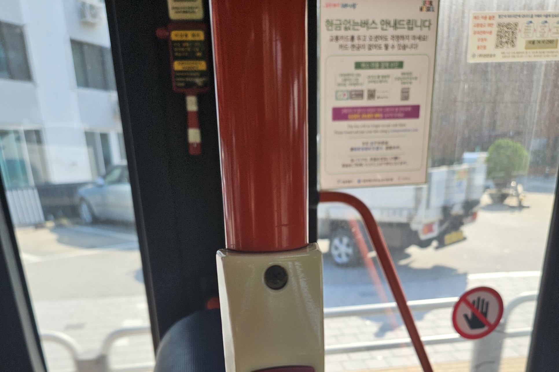 A notice headed 현금없는버스 안내드립니다 (cashless bus notice) on the window of a Seoul bus, next to a red handrail