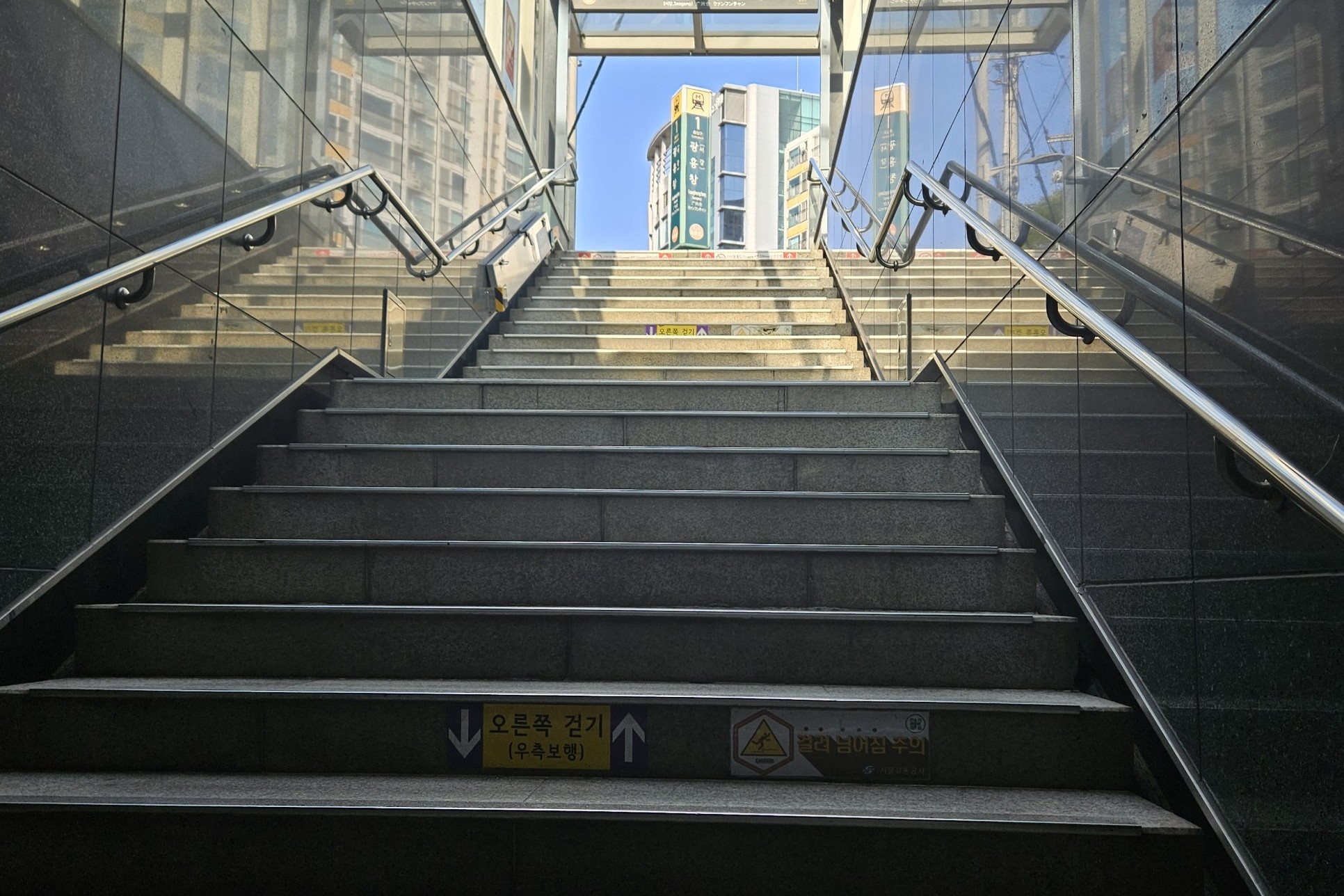Looking up a covered stairway from a Seoul subway station to the street at Gwangheungchang Station (광흥창역), with a keep-right sticker on one step