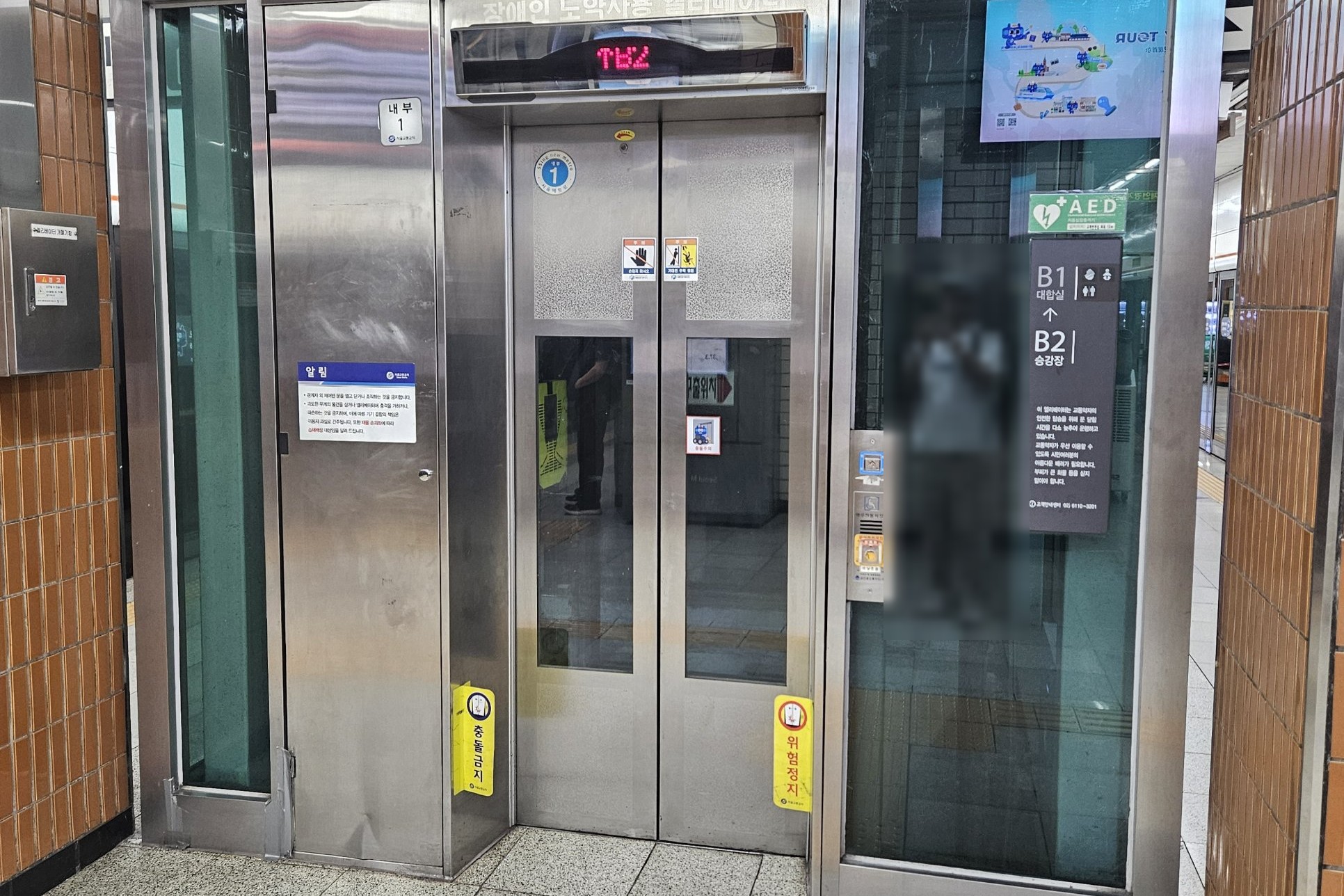 A glass-walled elevator on a Seoul subway platform with priority icons above the door and a sign reading B1 concourse, B2 platform