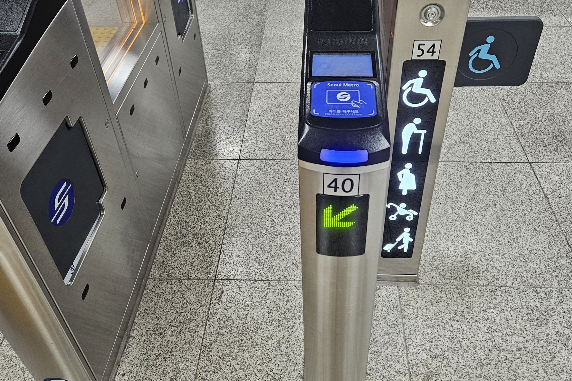 A Seoul Metro ticket gate next to a wider gate marked with icons for wheelchair users, older people, pregnant women, strollers and luggage