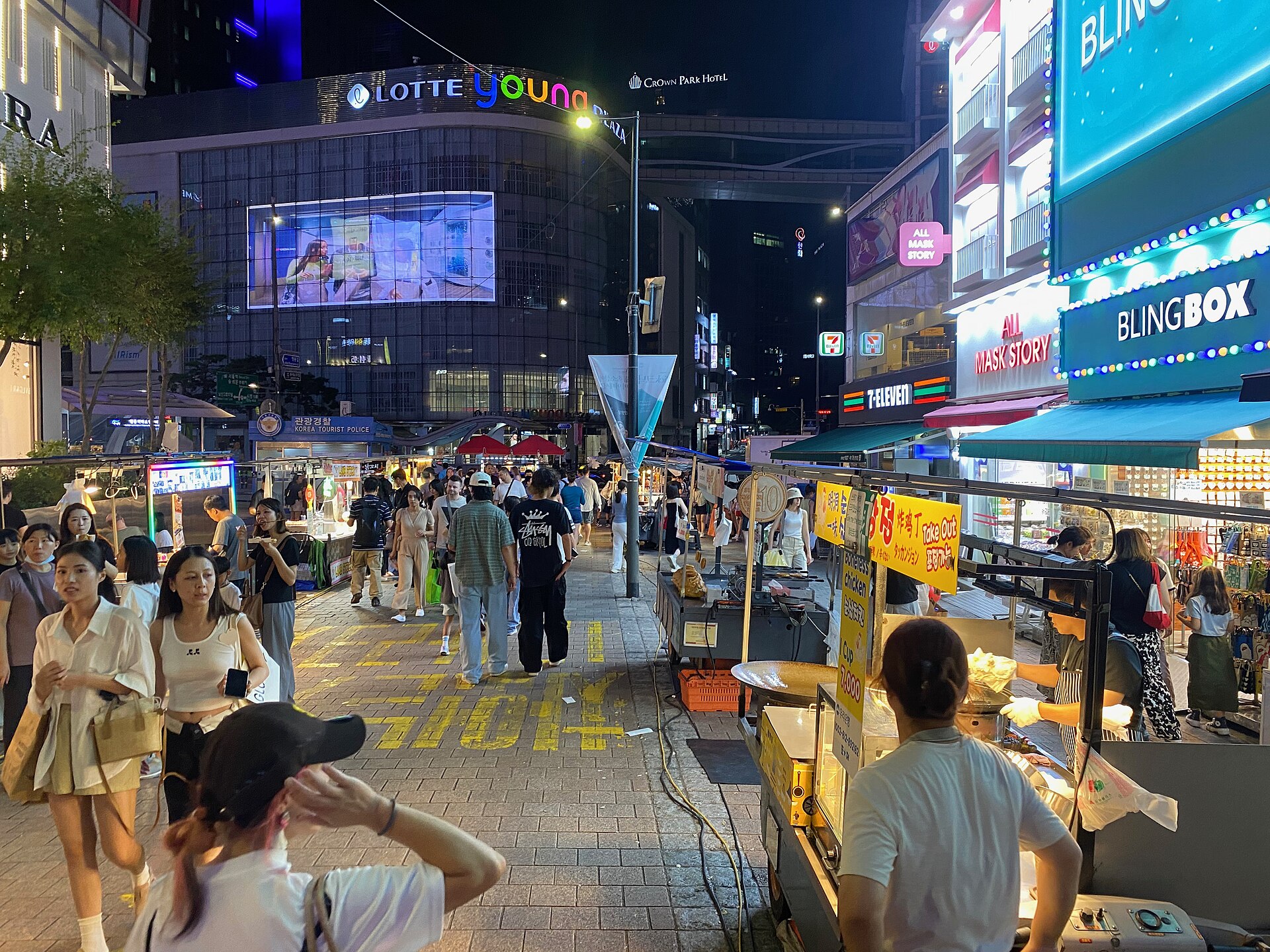 Crowds walking past street food stalls and shop signs on a Myeongdong street at night