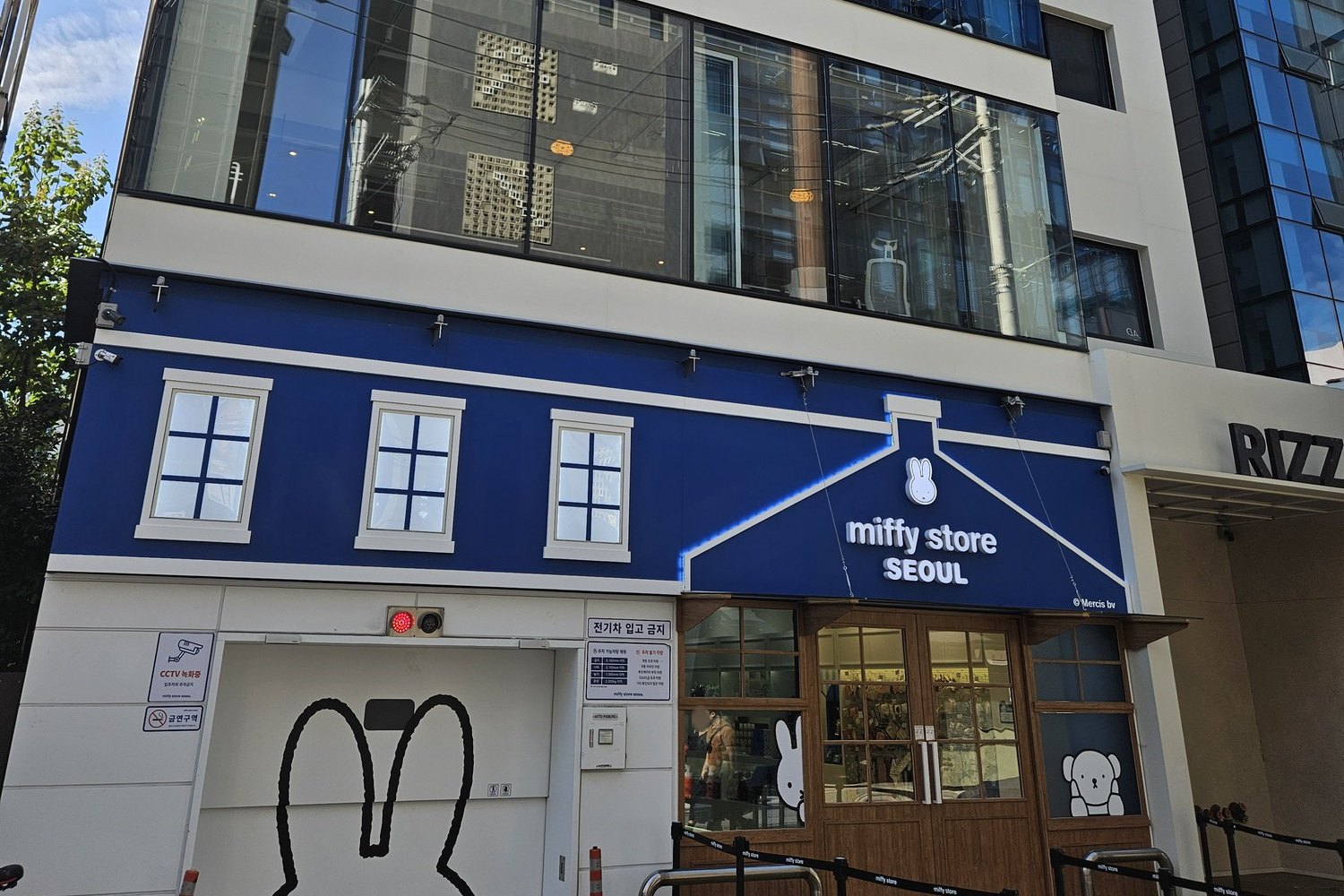 The blue and white front of Miffy Store Seoul with a Miffy outline on the wall and a queue barrier outside