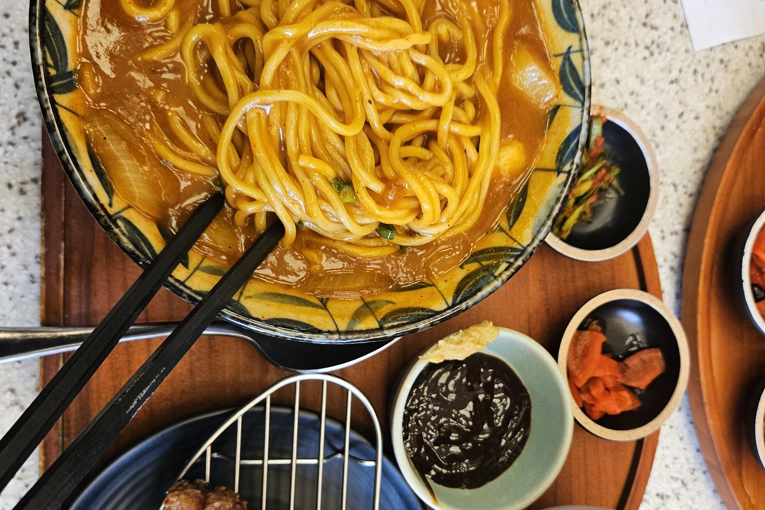 A bowl of thick curry udon with side dishes and rice on a wooden tray
