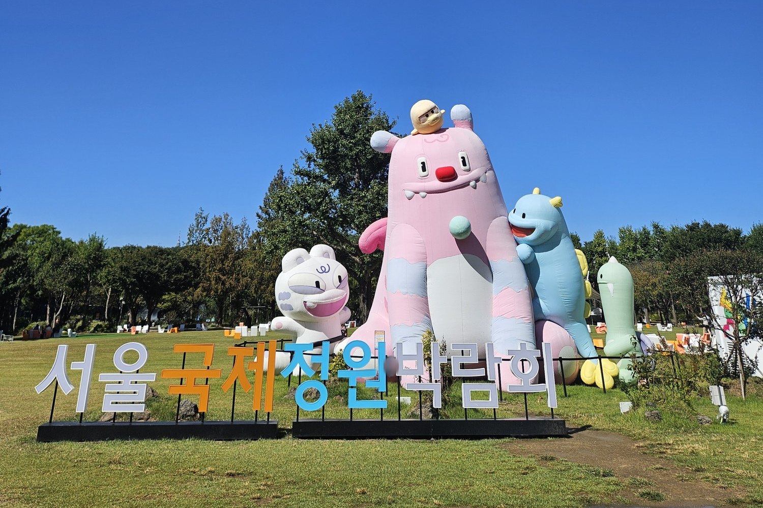 A giant inflatable Haechi with smaller characters on the lawn at Seoul Forest behind a Seoul International Garden Expo sign