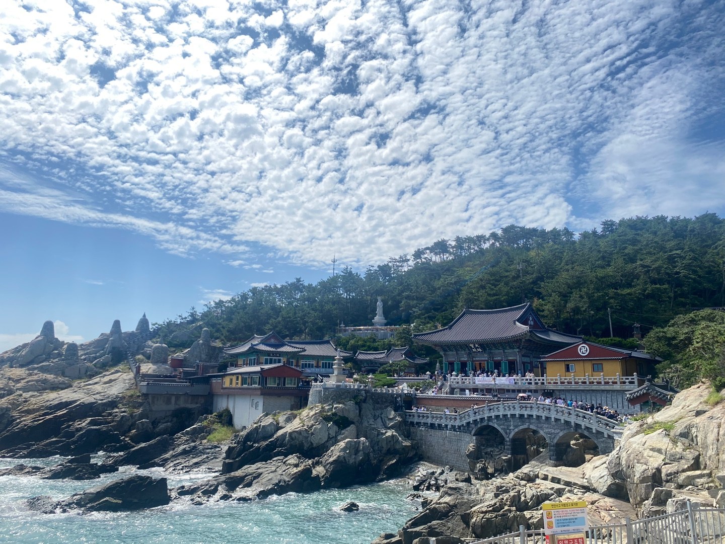 Haedong Yonggungsa Temple on rocks above the sea in Gijang, Busan, with a stone bridge and visitors on a sunny day