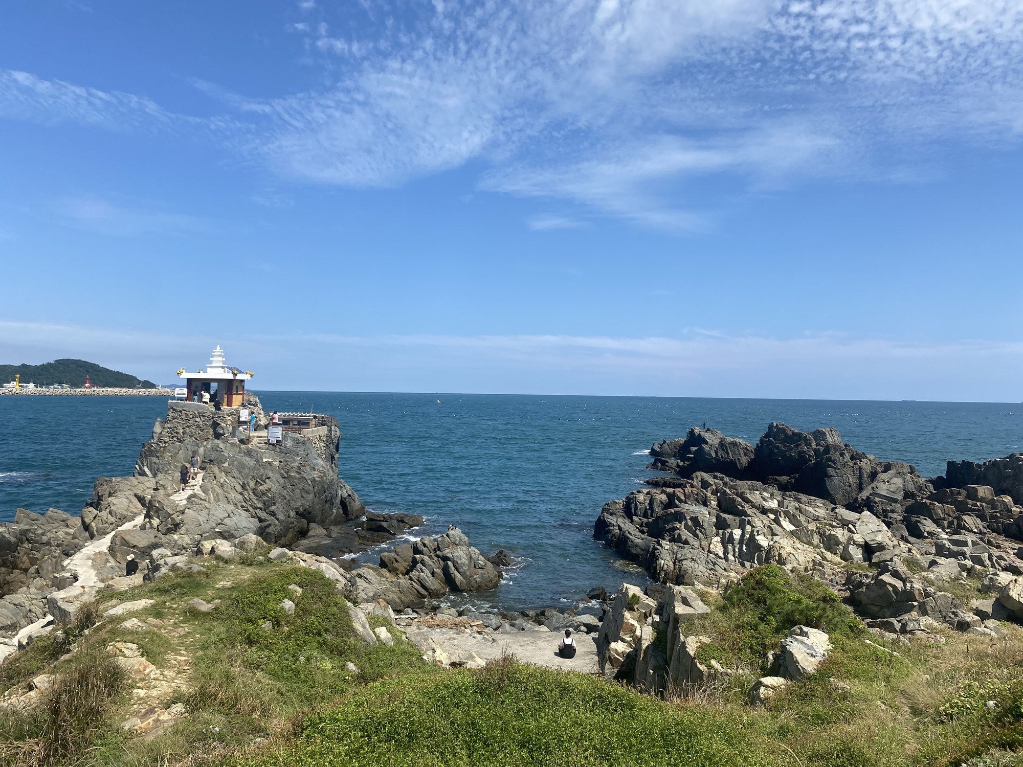 A small shrine with a white pagoda roof on a rocky point at Orangdae in Gijang, Busan, with blue sea and sky