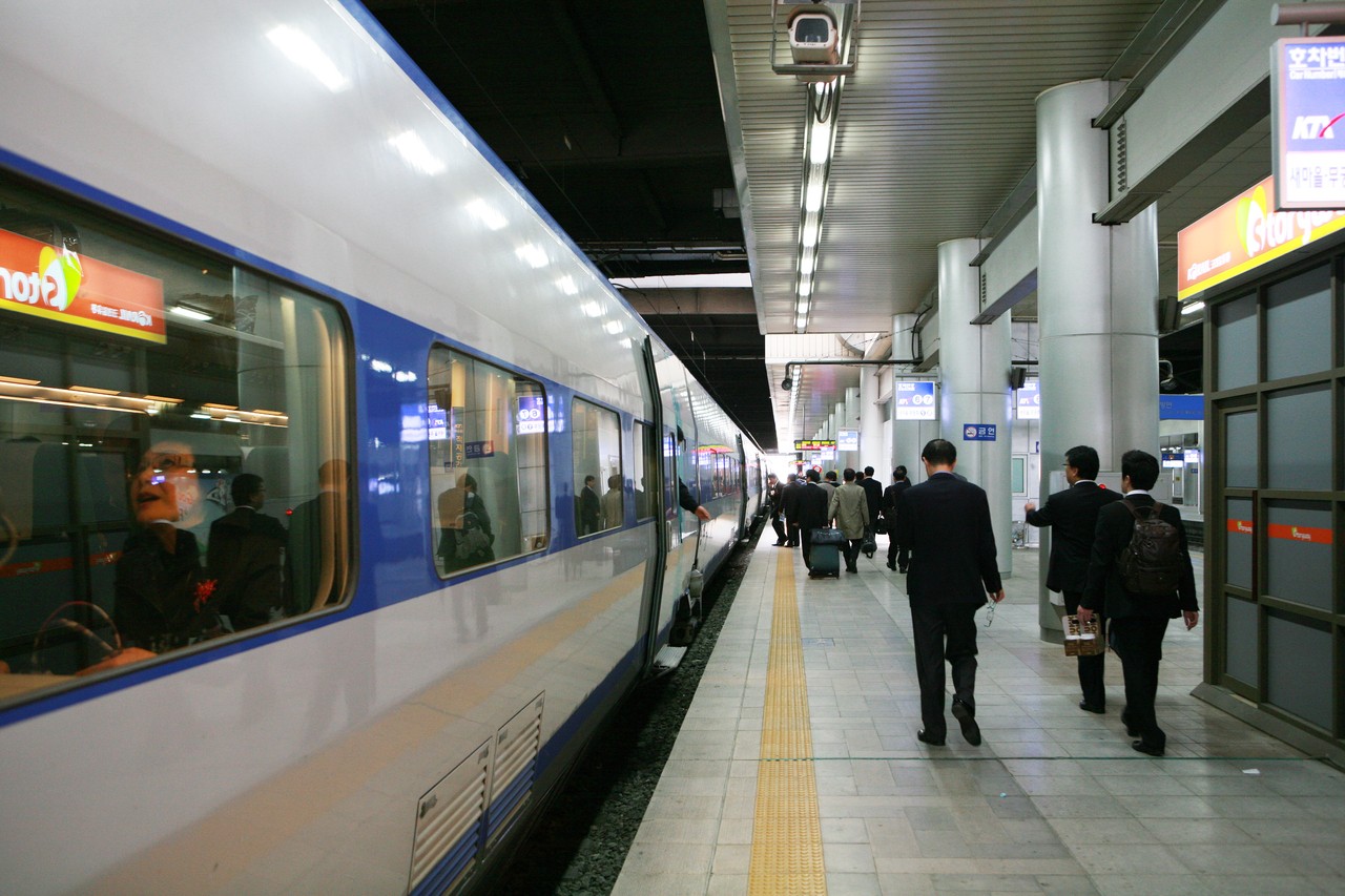 A white KTX train at a platform in Seoul Station with passengers walking along it
