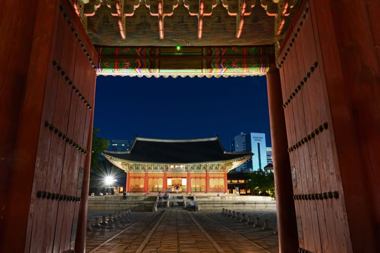 Junghwajeon hall at Deoksugung lit up at night, framed by the open wooden doors of Junghwamun gate