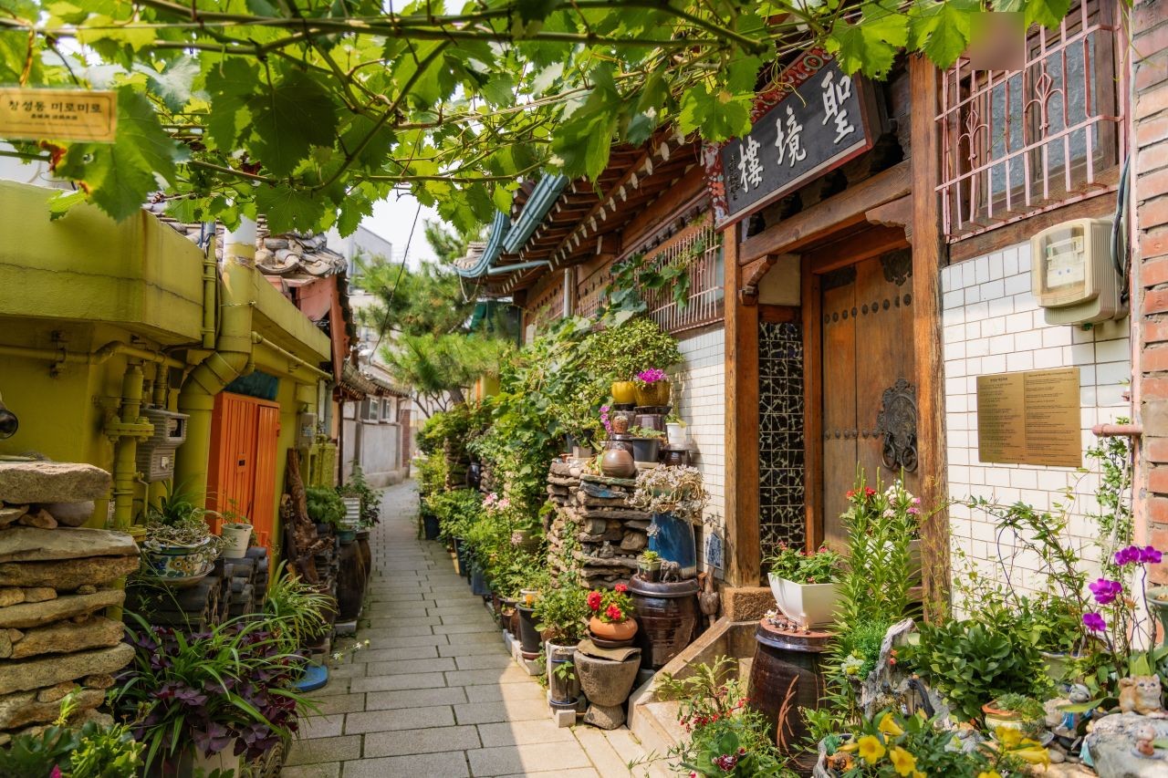 A narrow alley lined with potted plants and a hanok gate in the Seochon area of Jongno-gu