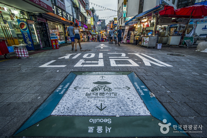 A floor sign in Namdaemun Market with the market name in Korean and English on the pavement of a busy lane