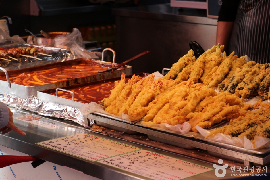 Trays of tteokbokki and fried snacks at a street-food stall in Namdaemun Market with a handwritten price board