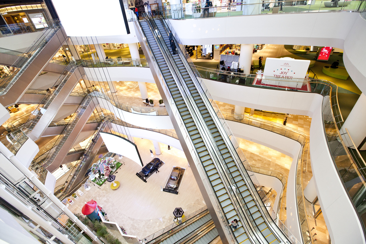 Escalators crossing a bright white multi-storey atrium inside Lotte World Mall in Jamsil
