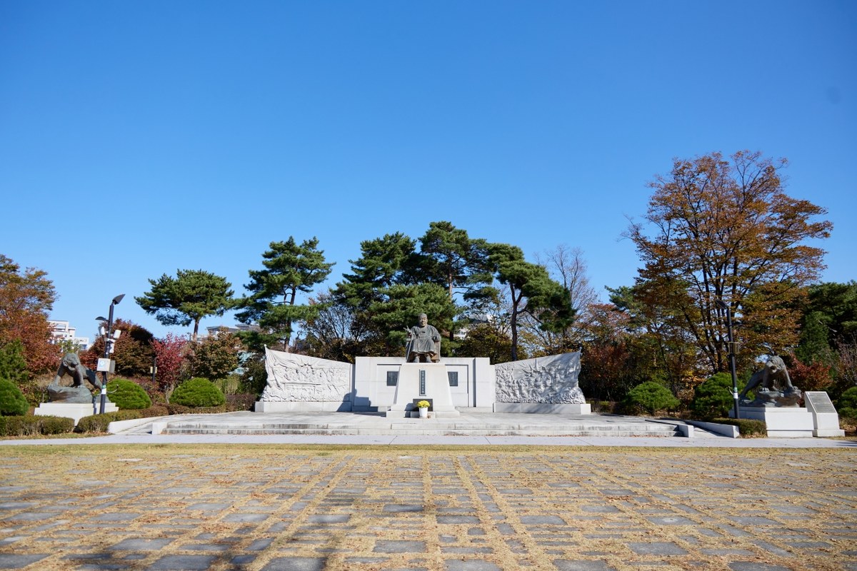 Baekbeom Square on Namsan in autumn with a memorial, pine trees and red and yellow leaves under a blue sky