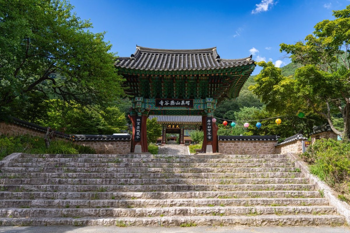Wooden entrance gate of Yeongoksa temple at the top of a stone staircase with green mountains behind