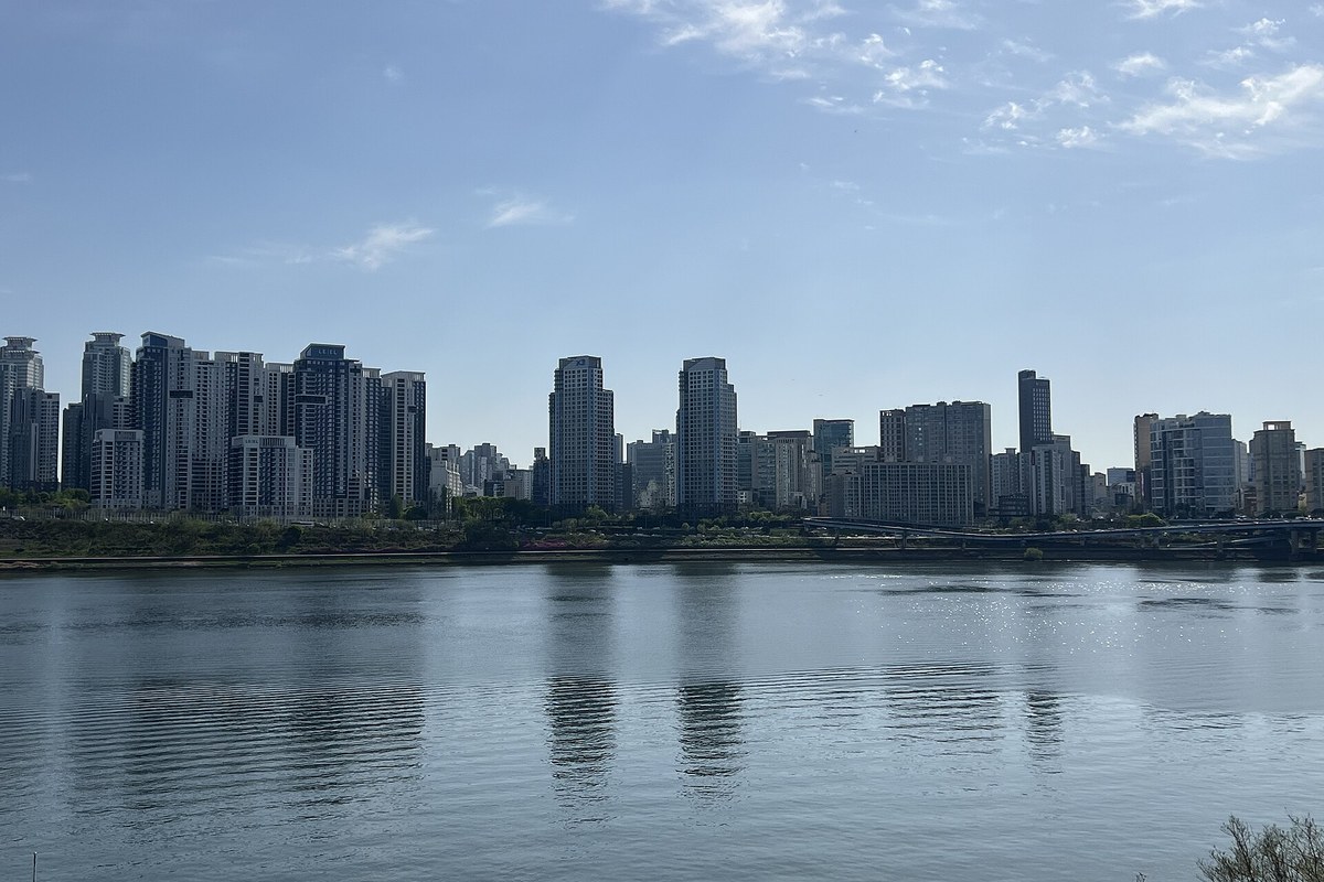 The Han River at Ttukseom with a row of high-rise apartment buildings on the far bank under a blue sky with thin clouds