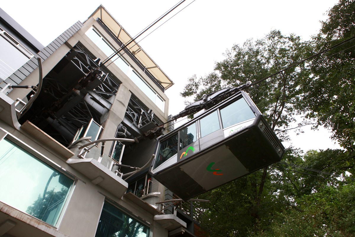 A Namsan Cable Car cabin leaving the upper level of the station building, with green trees behind it