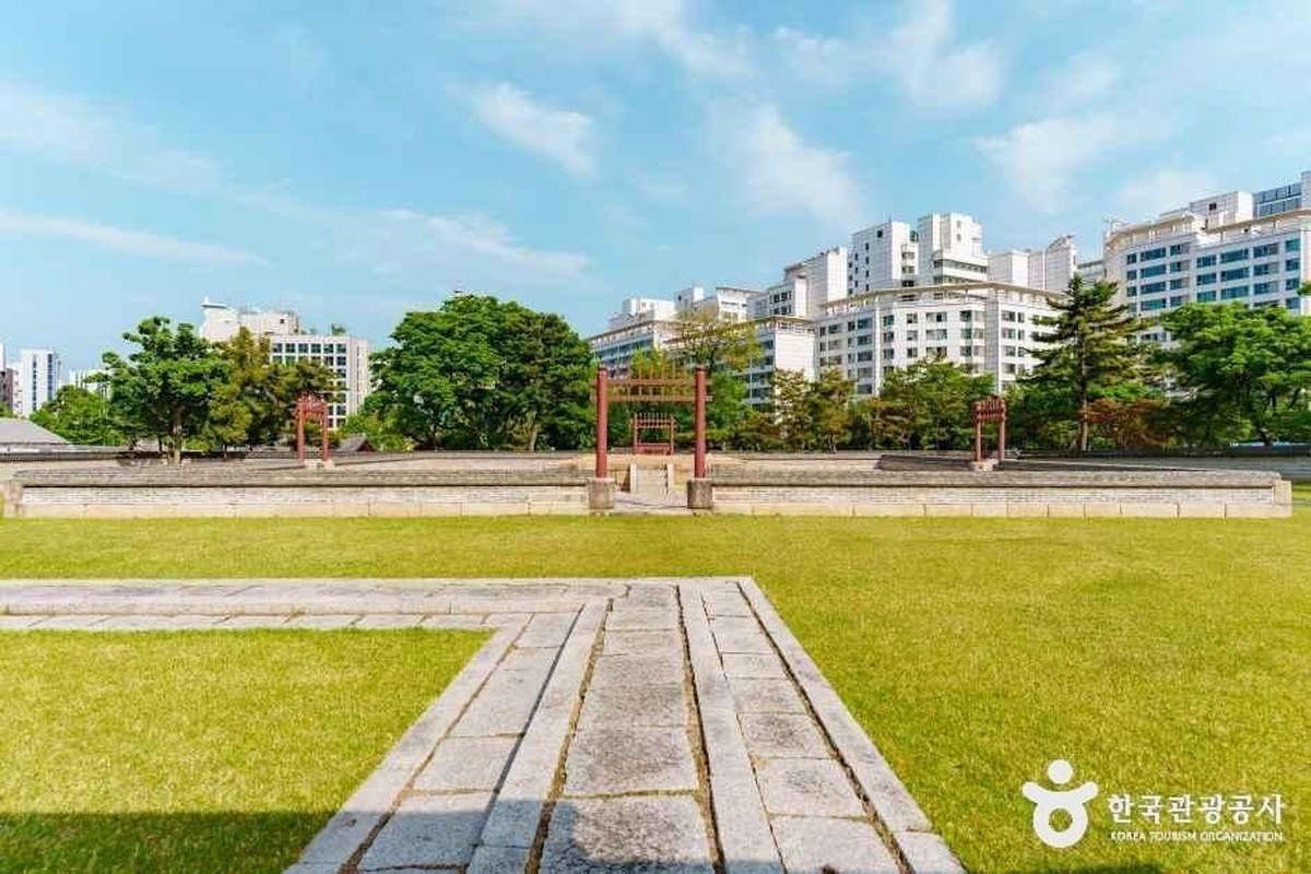 Sajikdan altar: a low stone platform on a green lawn with a red wooden gate and apartment buildings behind