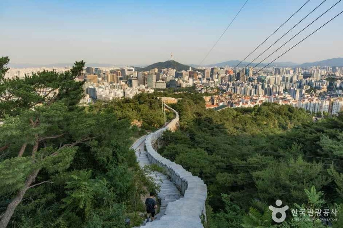 A stone-paved path along a fortress wall on Inwangsan with the Seoul skyline in the distance