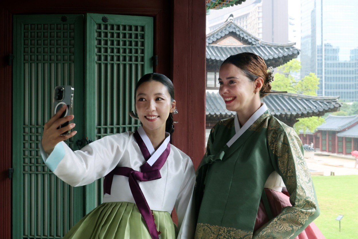 Two women in hanbok taking a selfie in front of green palace lattice doors during the proper hanbok campaign