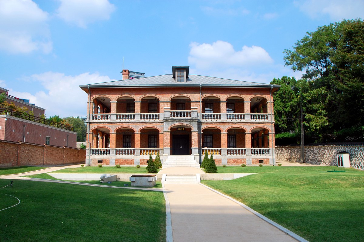 Two-story red-brick Jungmyeongjeon hall with arched balconies and a green lawn in front, seen in daylight
