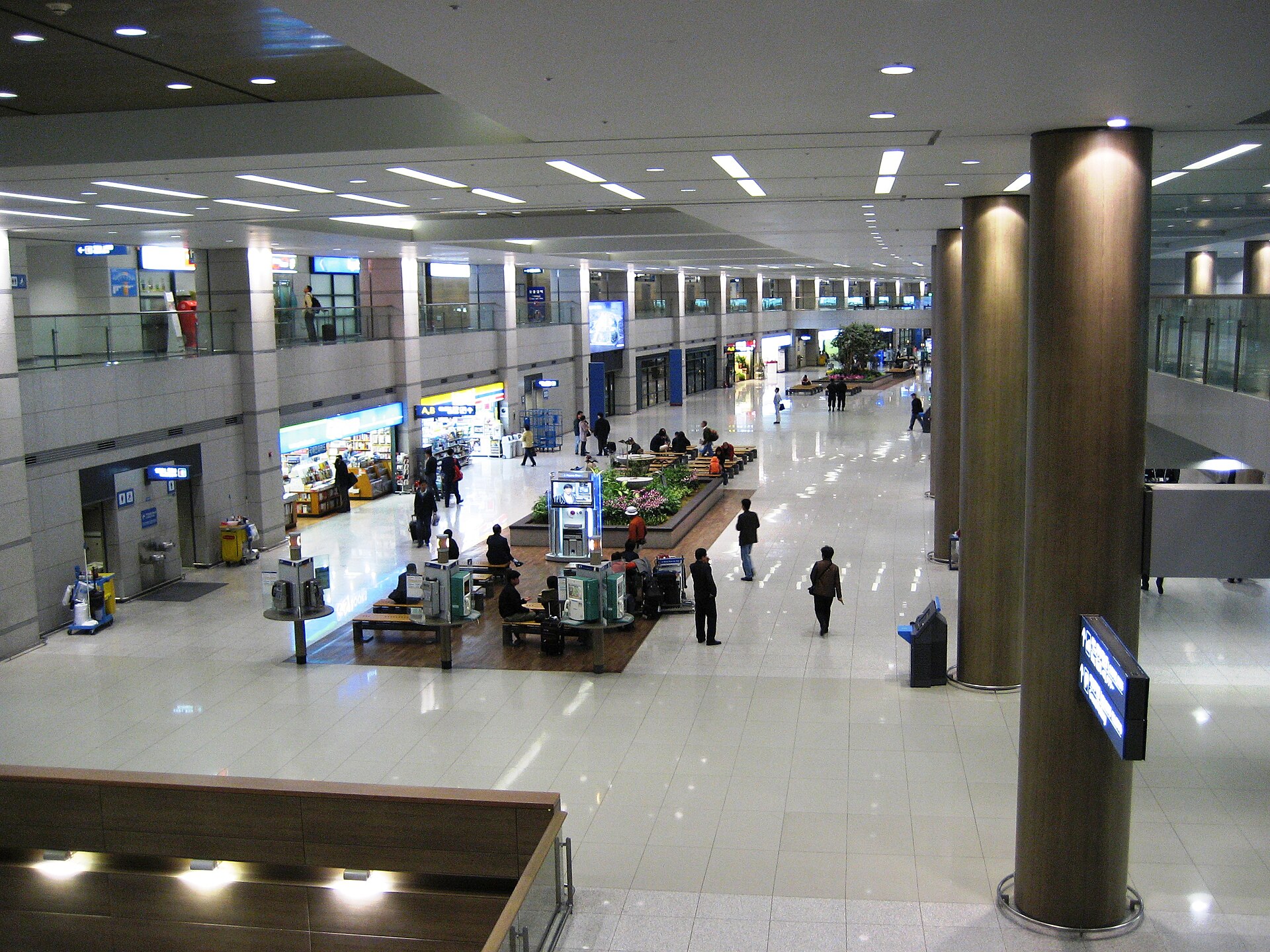 The arrival hall at Incheon International Airport seen from above, with a wide hall, shops along the side and a few travelers walking