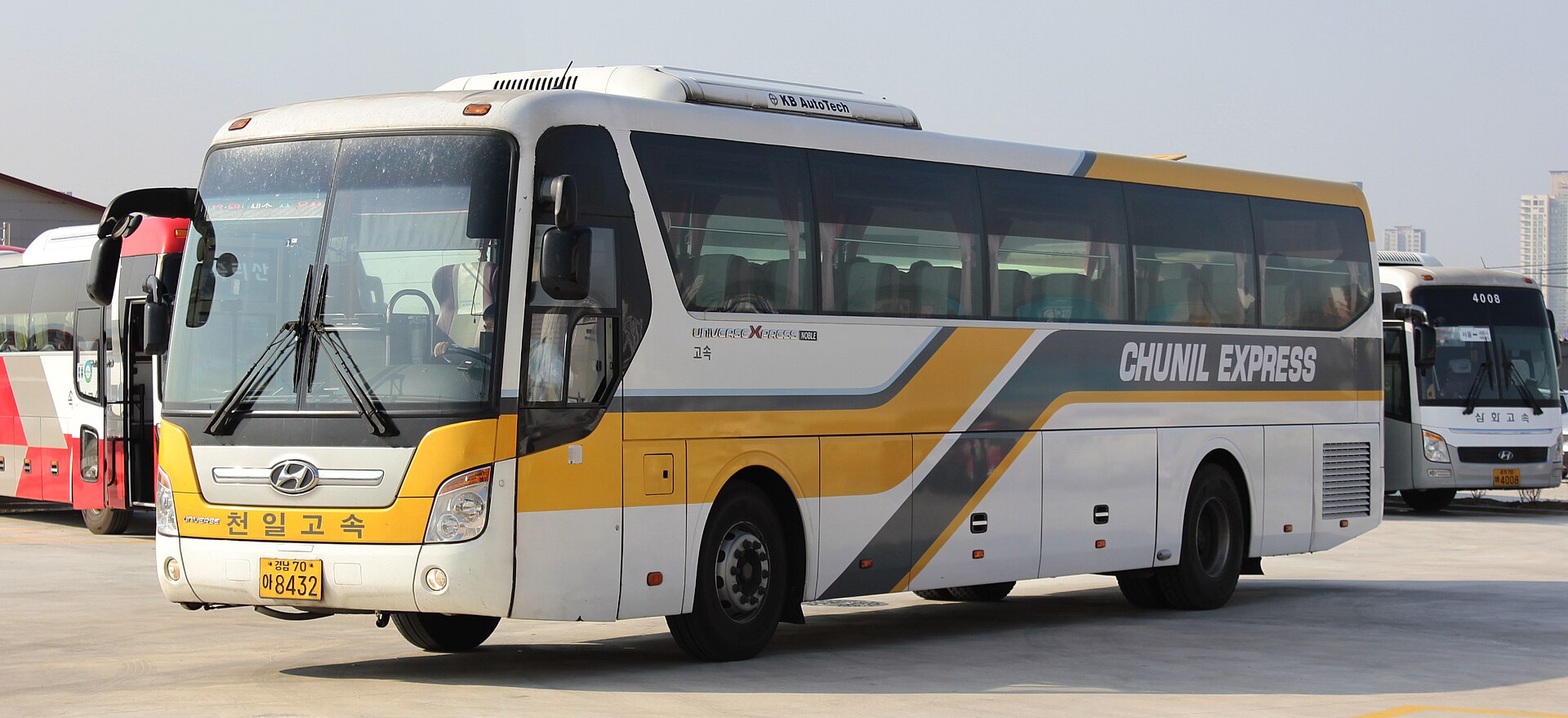 A white express coach with a yellow and grey stripe and the name Chunil Express on the side, parked at a bus terminal