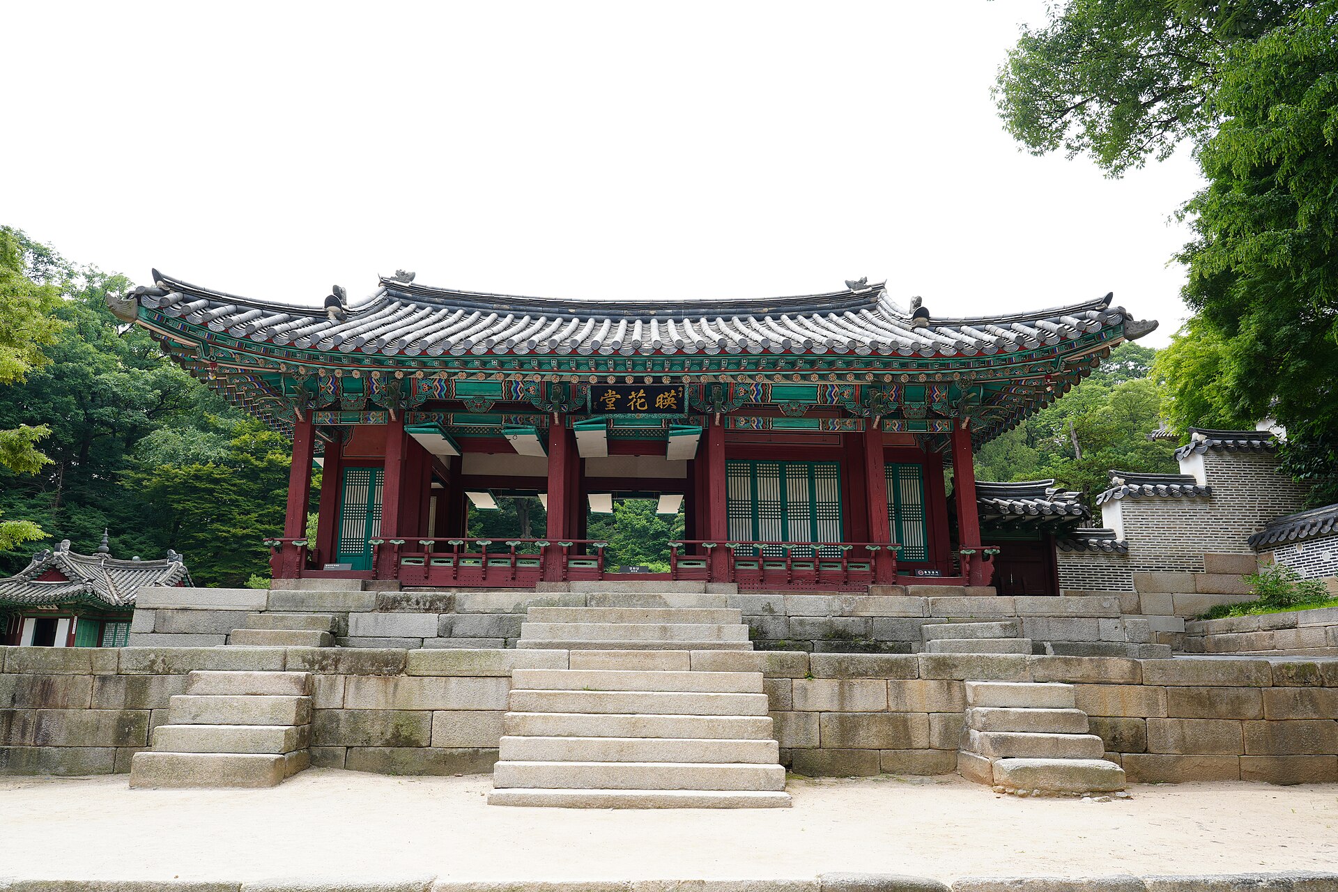 The front of Yeonghwadang hall in Changdeokgung's rear garden, with a wide stone stairway, red pillars and green trees behind