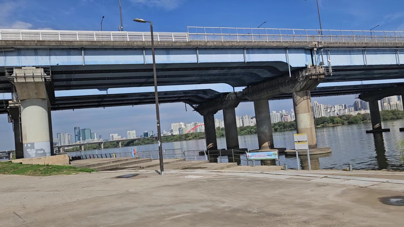 Concrete river path running under Mapo Bridge beside the Han River, with apartment blocks on the far bank