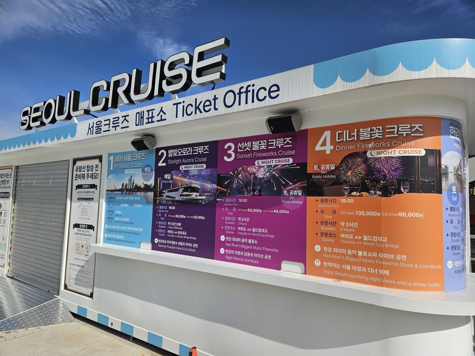 Seoul Cruise ticket office kiosk with a board listing four cruises in blue, pink, purple and orange panels with times and prices