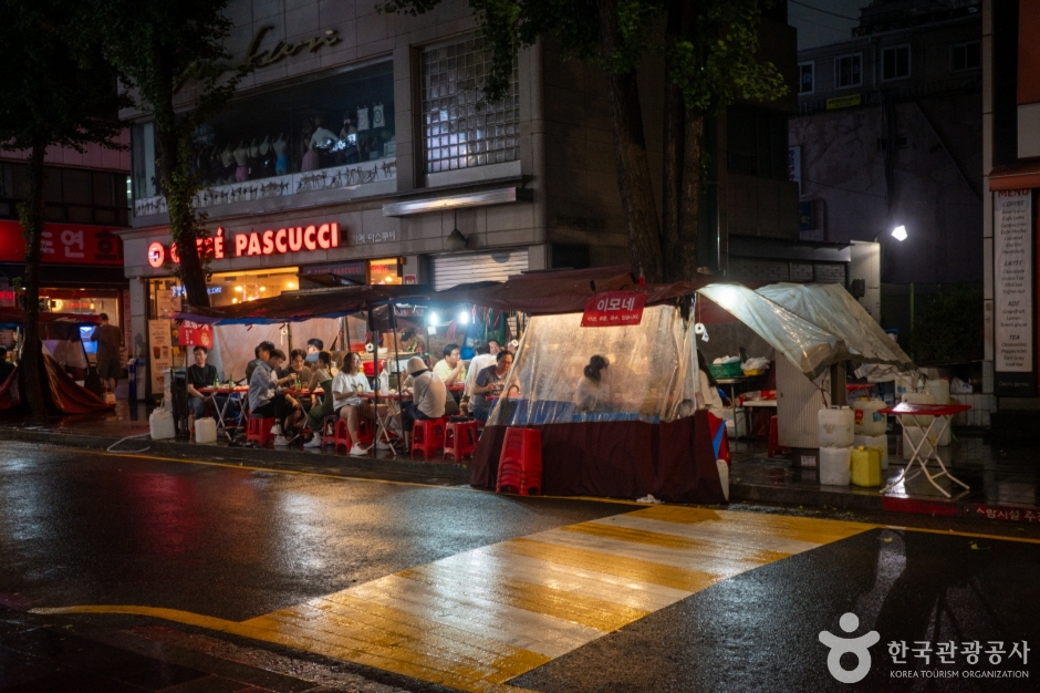 Pojangmacha tents with people sitting inside on a wet night in Gwansu-dong beside a Caffe Pascucci sign and a pedestrian crossing