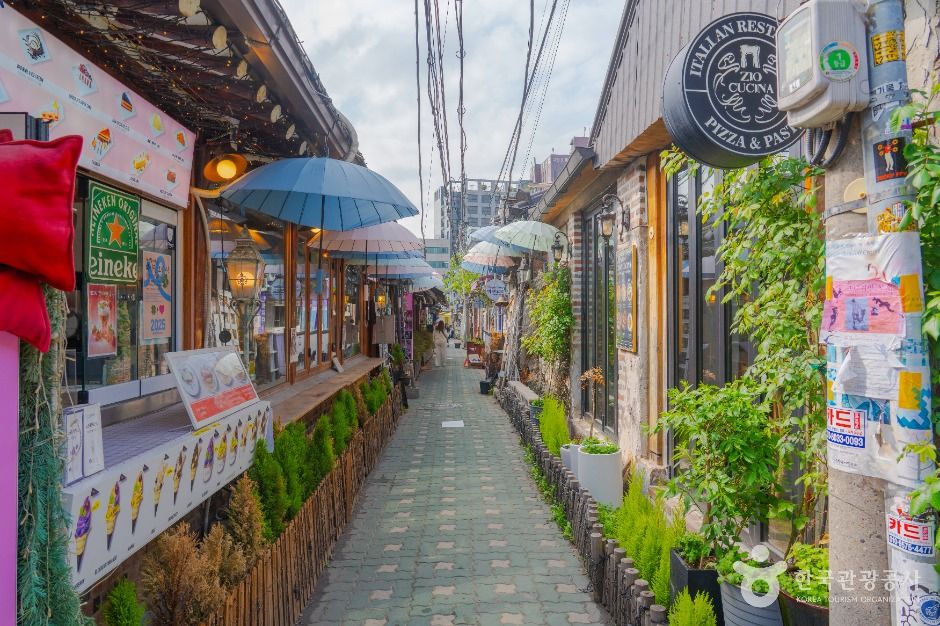 Narrow paved lane between renovated hanok buildings in Ikseon-dong with umbrellas strung overhead and plants along the walls