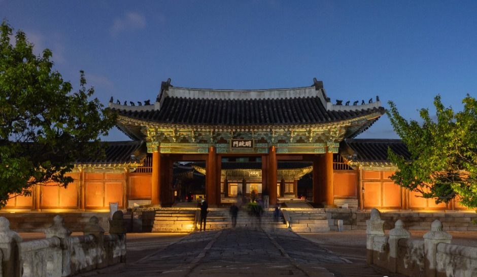 Honghwamun gate of Changgyeonggung palace in Seoul lit with warm lights at dusk, seen from the stone path in front