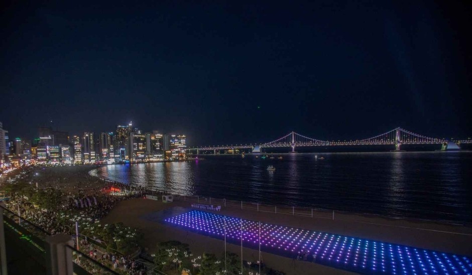 The Gwangan Bridge lit up over Gwangalli Beach at night with the city skyline along the shore