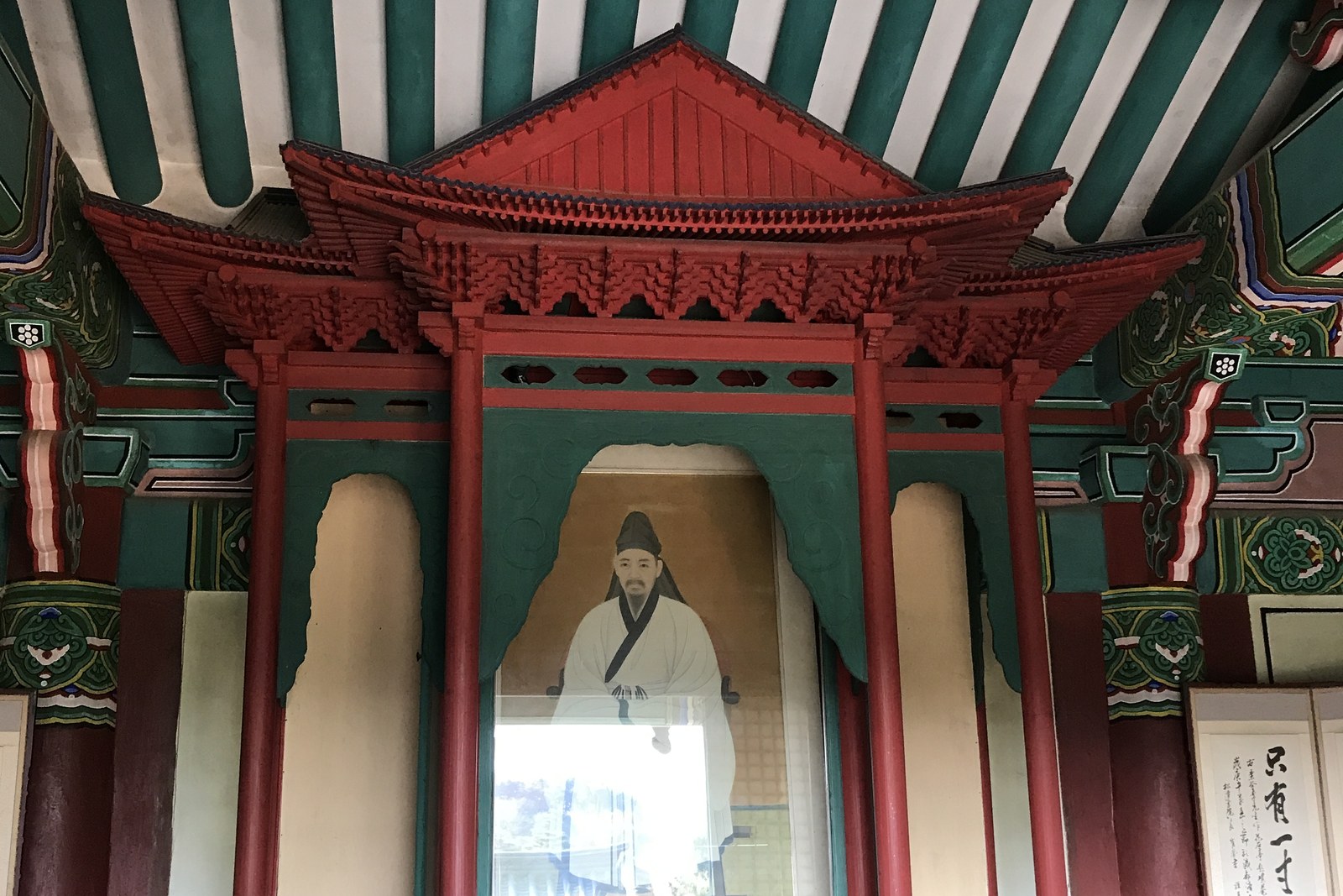 The painted red and green interior of a shrine hall with a portrait of a scholar in white robes at Ojukheon in Gangneung