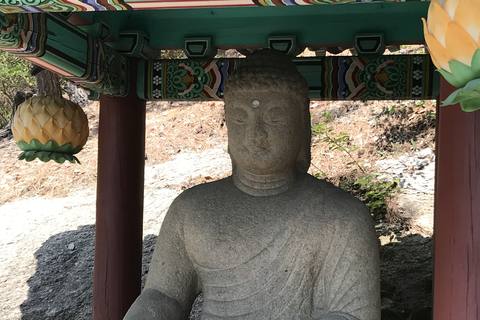 A seated stone Buddha under a painted wooden canopy with lotus lanterns