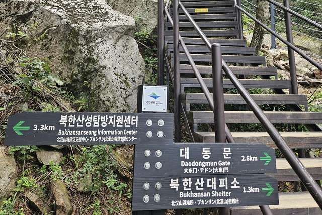 Wooden stairs and a green trail sign pointing to Daedongmun Gate and the shelter on a Bukhansan trail
